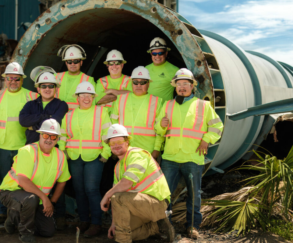 Group of workers in safety gear in front of large pipe.